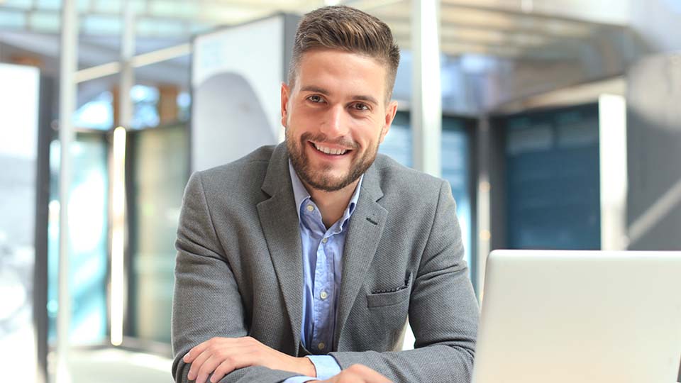 Mann sitzt an einem Laptop und lächelt