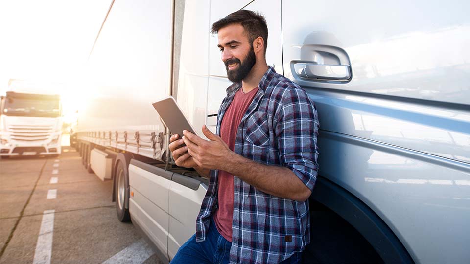 Mann steht vor einem Traktor und schaut auf sein Handy
