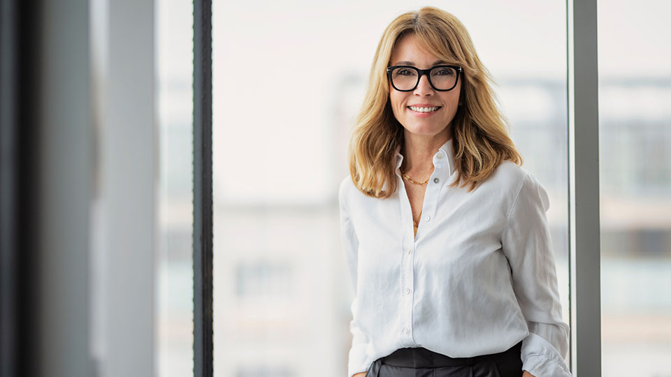 Eine Frau mit Brille schaut in eine Kamera und lächelt