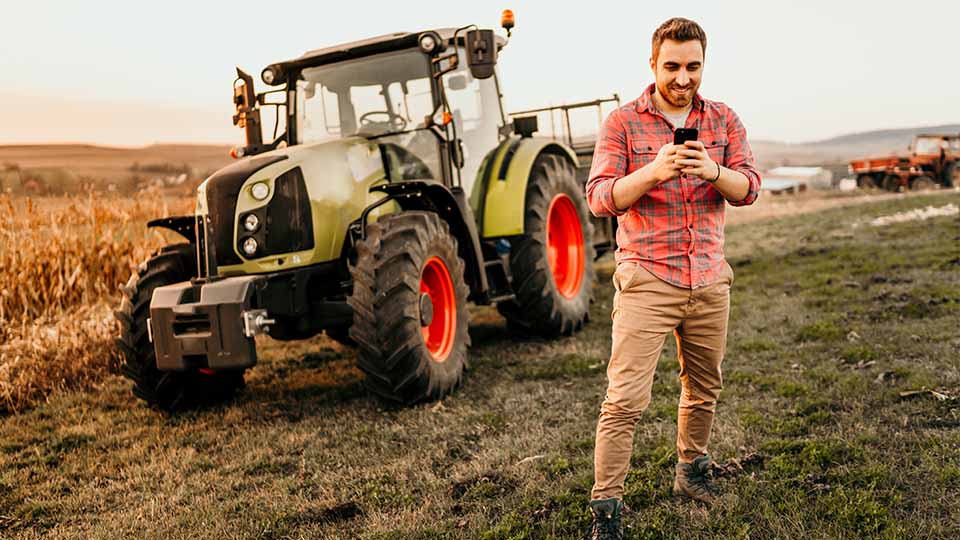 Mann steht vor einem Traktor und schaut auf sein Handy