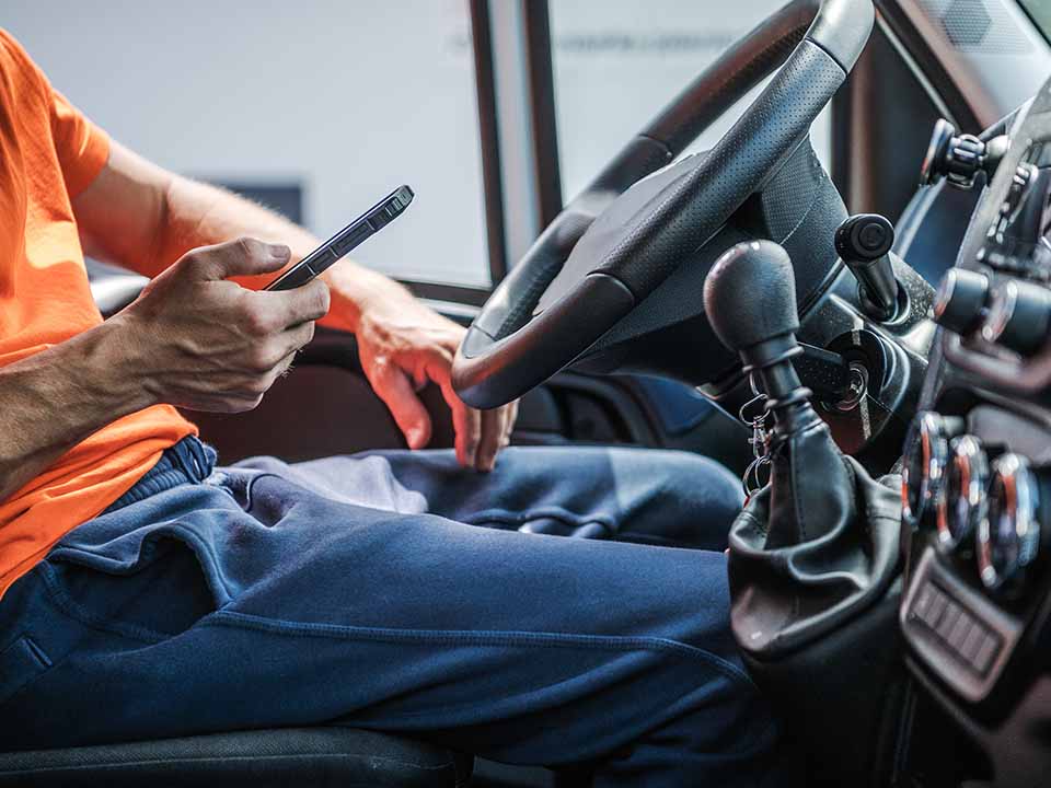 Mann sitzt in einem Auto und hat ein Handy in der Hand