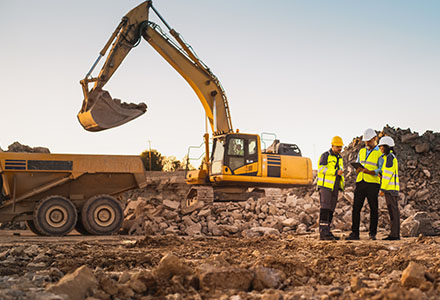 Drei menschen mit Warnweste stehen vor baumaschinen Bagger und Radlader