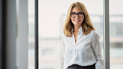 Eine Frau mit Brille schaut in eine Kamera und lächelt