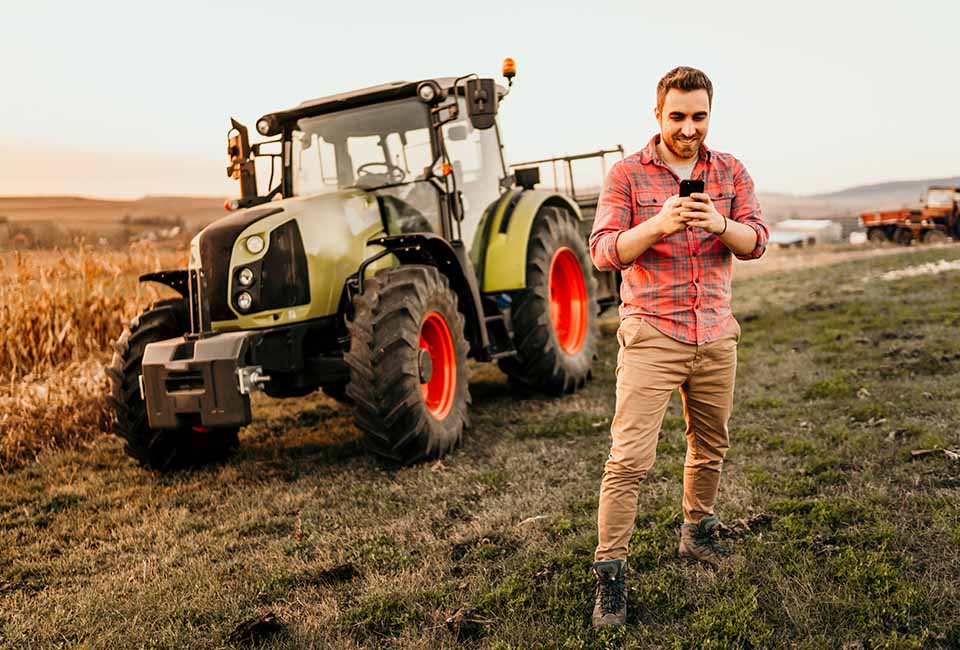 Mann steht vor einem Traktor und schaut auf sein Handy